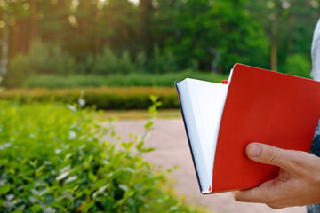 A man holds a book notebook in a green summer park - obrazy, fototapety, plakaty
