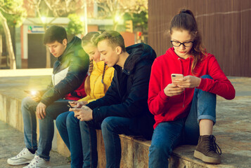 Four teenagers enthusiastically look at the screens of their smartphones on city street