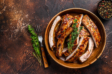 Cut BBQ grilled pork rack spareribs in a wooden plate. Dark background. Top view. Copy space