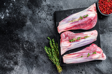 Raw lamb shanks meat on a marble board. Black background. Top view. Copy space