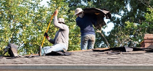 Constructioin workers removing roof shingles on a residential house
