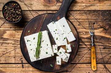 Cut cheese feta with rosemary on a wooden cutting board. wooden background. Top view - obrazy, fototapety, plakaty