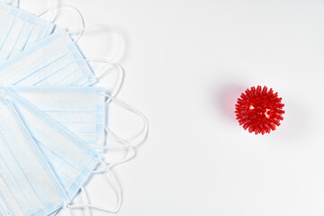 medicine, healthcare and pharmacy concept - many blue disposable medical masks and red coronavirus spike massage ball on a white background. Copy space. Flatlay