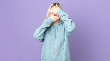 pretty albino woman covering face with both hands saying no to the camera! refusing pictures or...