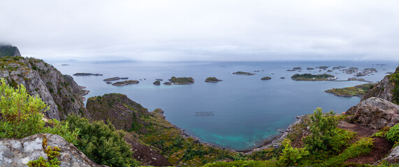 Wide panoramic view from top of cliff on the ocean and on blue panorama of mountains and Reine in...