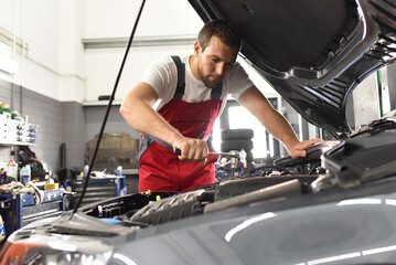 Fototapeta na wymiar car mechanic in work clothes works in a workshop and repairs a vehicle