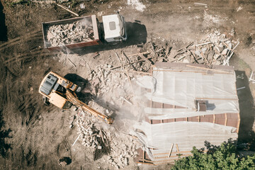 Excavator with bucket breaks house. Demolition of building, top view from drone.