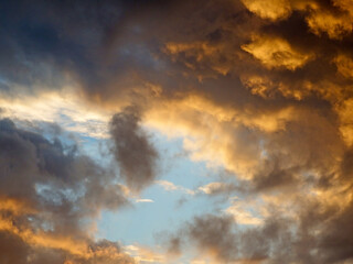 Skyscape background of a changing sky with dark and orange sunlit clouds gathering