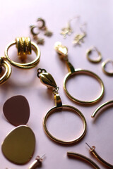 Various gold earrings on pastel pink background. Selective focus.
