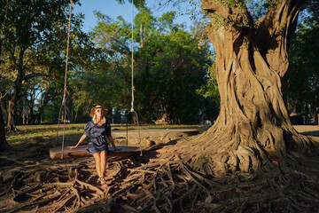 Vacation concept. Happy young woman in hat sitting in swing.