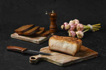 Fototapeta na wymiar Smoked lard with brown bread on wooden cutting board