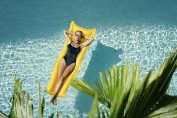 Enjoying suntan. Tropical vacation concept. Top view of young woman on the yellow air mattress in...