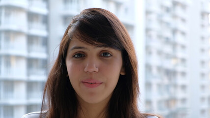 Closeup of a young South Asian female smiling at the camera with blurry buildings in the background