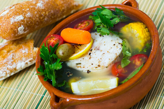 Fisher soup from merluccius. Recipe: boil broth from fish head, add potatoes, carrots, shallots, corn, fish fillets or steak 200 g, season with salt, pepper. Then cook in oven at 200 deg for 40min