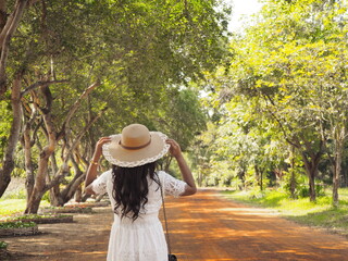woman in white dress catch the hat and stand on the road with tree around,Asian traveler girl with...