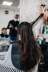 Young girl enjoying at hairstyle treatment while professional hairdresser gently working and cutting her hair.
