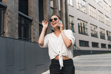 Fototapeta premium Close up emotion girl walking with smartphone in urban background. Smiling lady holding cellphone in hands outside. 