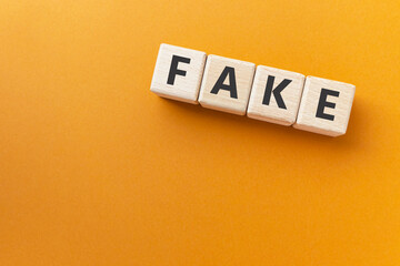 Text FAKE on wooden cubes on bright orange ocher background.  Not genuine, counterfeit. Square wood...