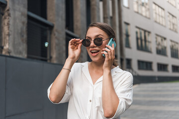 Business lady in eyeglasses and office clothing talking on smartphone while walking at big city. Charming female with brown hair having working conversation on mobile.