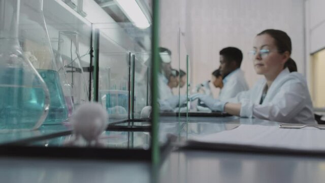 Close up shot with rack focus from female scientist in white coat working on computer and observing white lab rat in glass tank