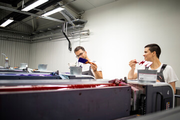 Printing machine operators working together with paint in print shop.