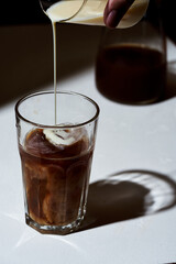 Milk is poured into a glass with thai cold iced tea standing on the white table top view 45 view