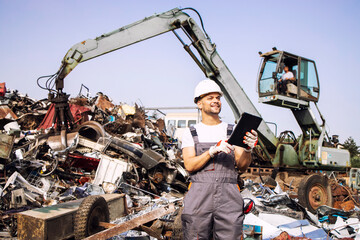 Man controlling process of industrial scrap metal recycling at junk yard.