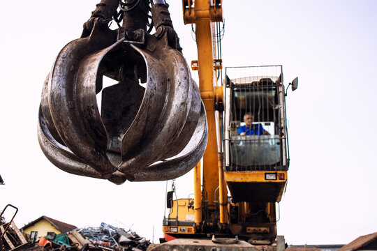 Man operating excavator industrial machine with claw attachment used for lifting scrap metal in junk yard.