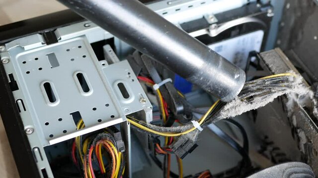 Removing dust buildup on the power cords with a vacuum cleaner. Dusting off the components of system unit case. Person is cleaning the inside of the computer