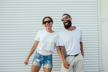 Young smiling couple in blank white t-shirts on street. Mockup for design. - Powered by Adobe