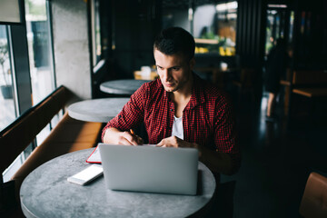 Skilled male copywriter with education textbook watching informative webinar on modern laptop...