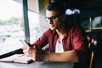 Caucasian hipster guy with education textbook writing email message via application on modern...