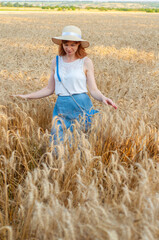 Woman with golden brown hair walks through a beautiful golden wheat field, hot summer season. Happy girl with hat enjoying life