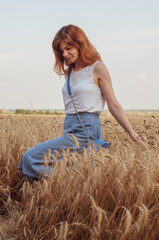 Naklejka na ściany i meble Woman with golden brown hair walks through beautiful golden wheat field, hot summer season. Happy girl enjoying life
