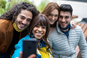 moment of selfie photos to the mobile of friends, group of young adults having fun, period of epidemic and use facial masks, focus on brazilian woman and caucasian man