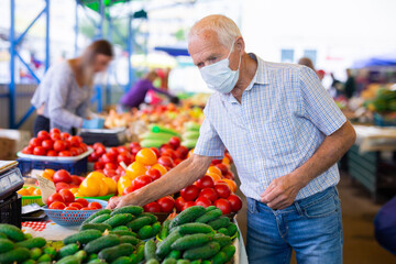 retired european man wearing medical mask protecting against the virus buying cucumbers and tomatoes in market
