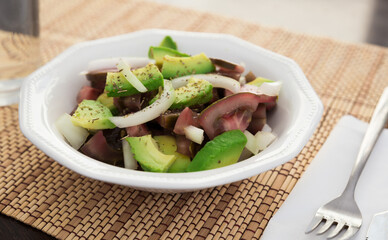 salad of black tomatoes, avocado and onions in white ceramic bowl