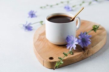 Obraz na płótnie Canvas Chicory drink in a white mug with chicory flowers next to it on a wooden board.
