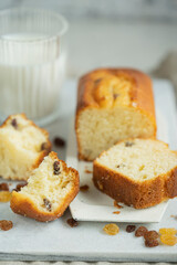 Homemade freshly baked butter sponge cake with raisins on white table with glass of milk. Sweet bakery - beautiful breakfast, macro shot, close up view with copy space. Biscuit dessert.