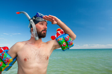 a man with a beard in a snorkeling mask and snorkel stands wet in the sea in the summer