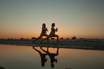 young women doing yoga on the seashore in the summer