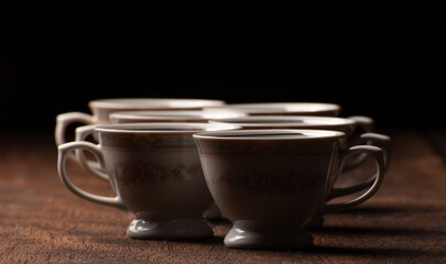 Porcelain cups, beautiful porcelain cups geometrically arranged on rustic wood, dark background, selective focus.