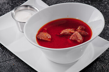 Homemade Russian, Ukrainian and Polish national soup - red borscht made of beetroot, vegetables and meat with sour cream. On textured dark background . High quality photo
