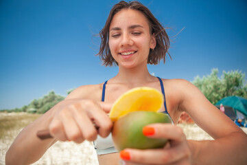 a young woman on the seaside cuts a piece of mango with a knife in the summer