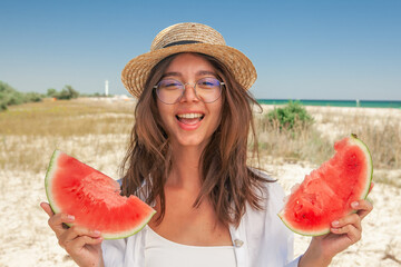 young woman in glasses and a straw hat eating fresh watermelon on the background of the sea coast in the summer