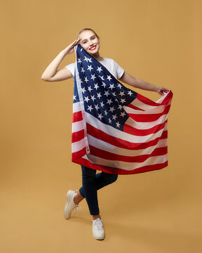 attractive blonde proudly poses with an American flag. photo shoot in the studio on a yellow background