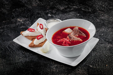 Homemade Russian, Ukrainian and Polish national soup - red borscht made of beetroot, vegetables and meat with sour cream. On textured dark background . High quality photo