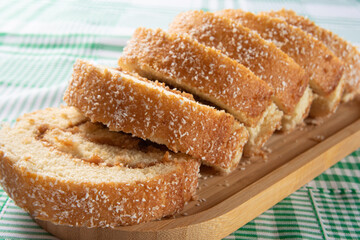 Rocambole, Sliced ​​rocambole stuffed with dulce de leche on a wooden tray on a table with checkered tablecloth. dark background, selective focus.