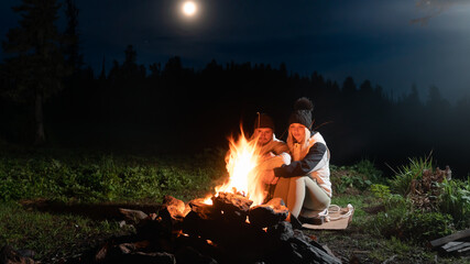 a couple in love is sitting at night by a campfire in the forest. Romantic evening, the concept of tourism by the fire