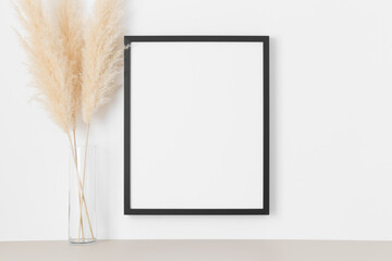 Black frame mockup on the wall with a pampas decoration.